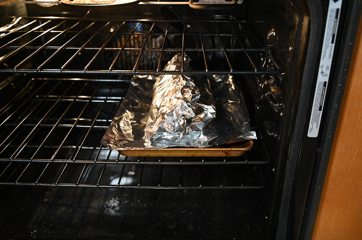 Image of the turkey breast wrapped in foil being cooked in the oven on a baking tray.