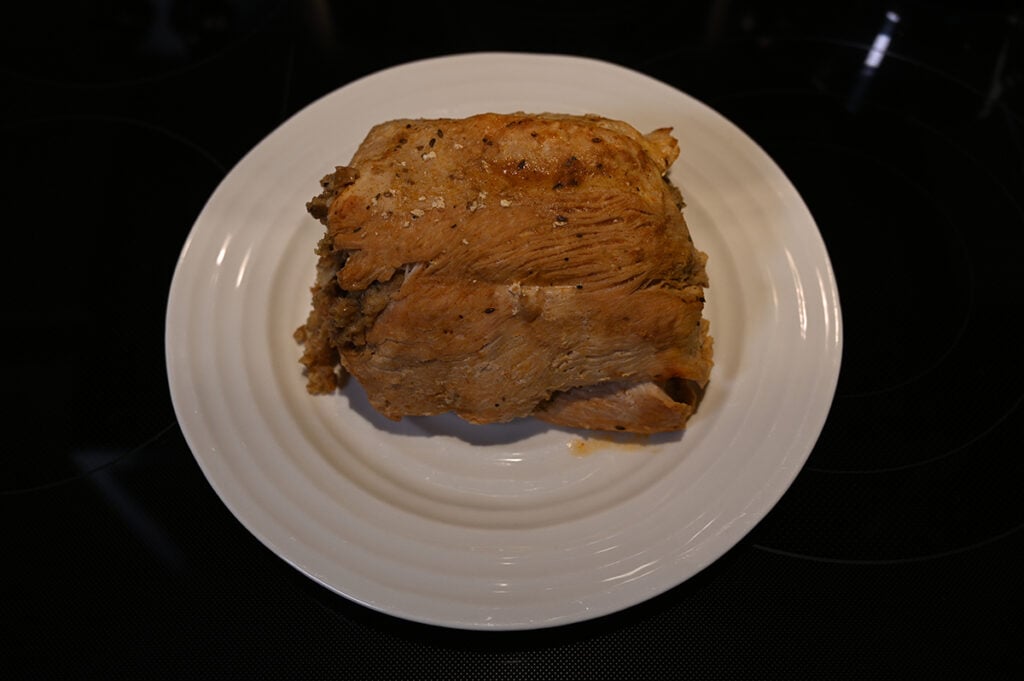 Image of the whole cooked stuffed turkey breast served on a white plate without chutney on top. 