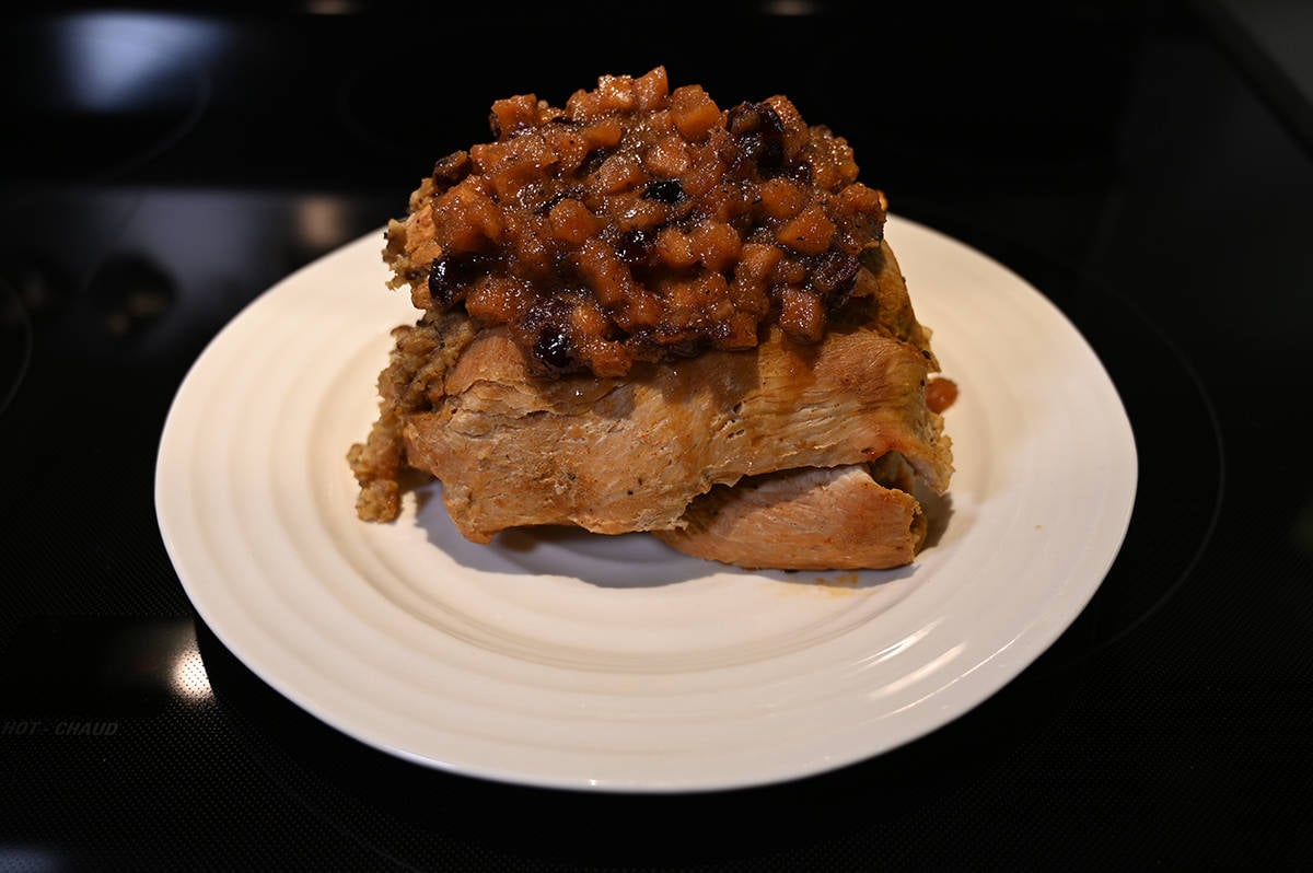 Image of the whole cooked stuffed turkey breast served on a white plate with chutney on top. 