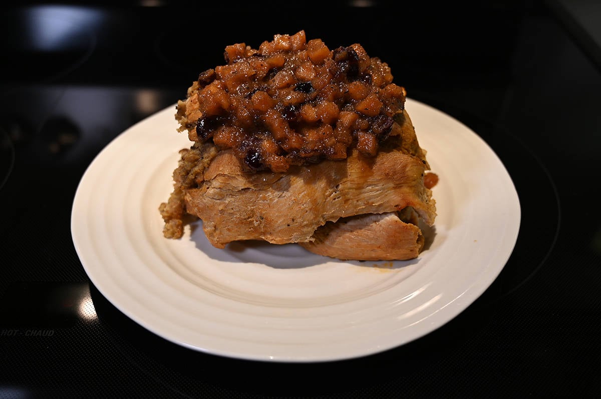 Image of the whole cooked stuffed turkey breast served on a white plate with chutney on top. 