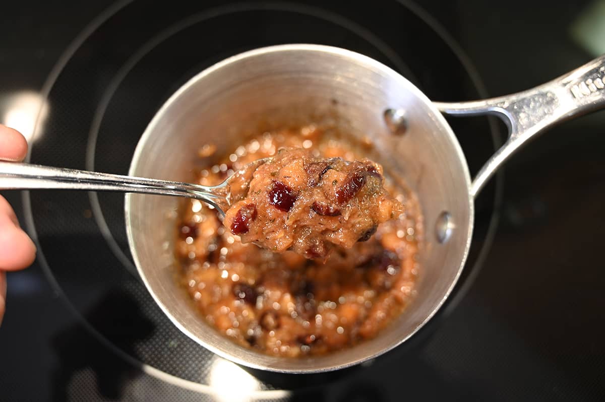 Closeup image of a spoonful of chutney close to the camera, behind the spoon is a pot of chutney on a stovetop.