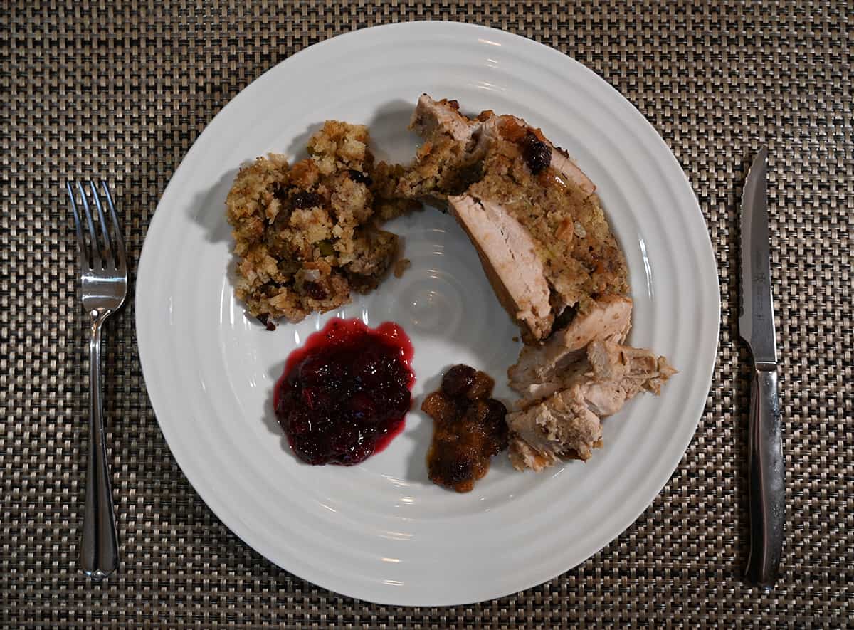 Top down image of a white plate with turkey breast, cranberry sauce and stuffing on it beside a knife and fork.