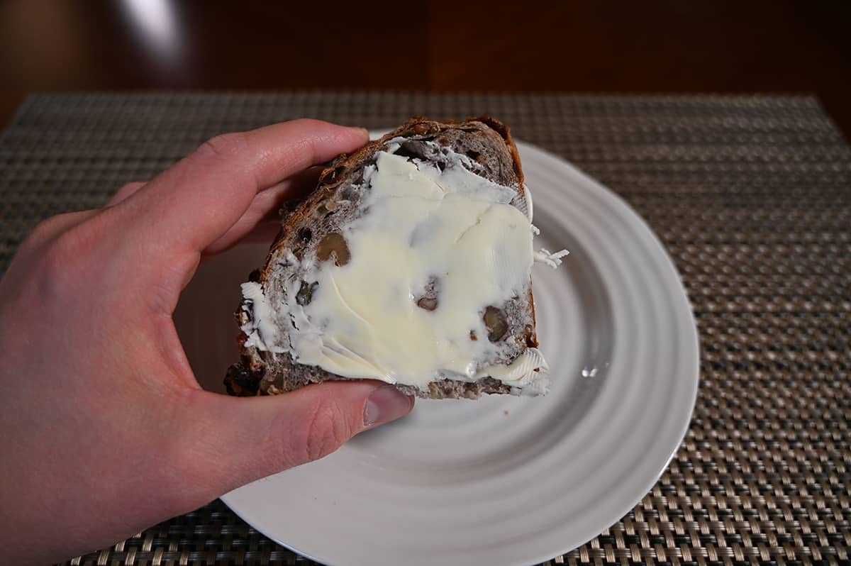 Closeup image of a hand holding one slice of cranberry walnut bread with butter on it close to the camera.