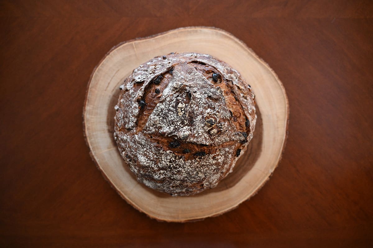 Top down image of the whole loaf of cranberry walnut bread sitting on a wooden cutting board. The loaf is round.