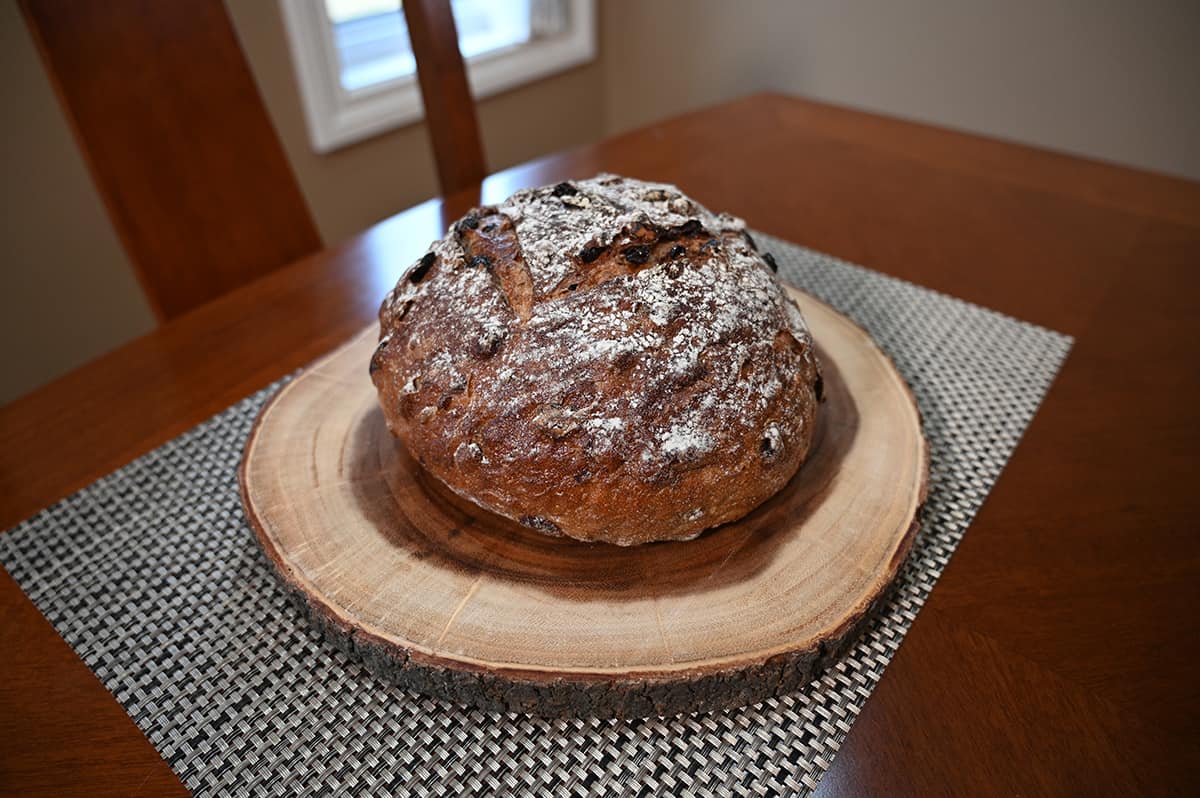 Side view top down image of the cranberry walnut bread from Costco unwrapped and sitting on a cutting board, it appears dusted with flour and crusty on the outside.