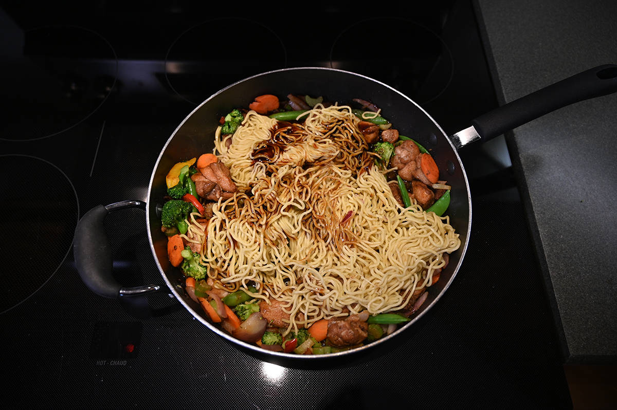 Top down image of the vegetables, chicken and noodles from the yakisoba being cooked in a frying pan on the stovetop.