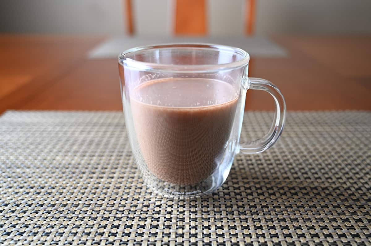 Image of a clear mug filled with milk chocolate hot cocoa sitting on a table.
