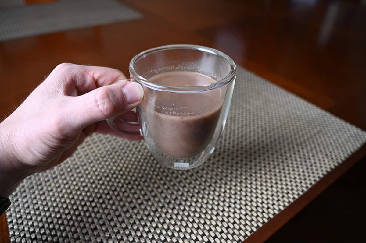 Closeup image of a hand holding a clear mug filled with milk chocolate cocoa.