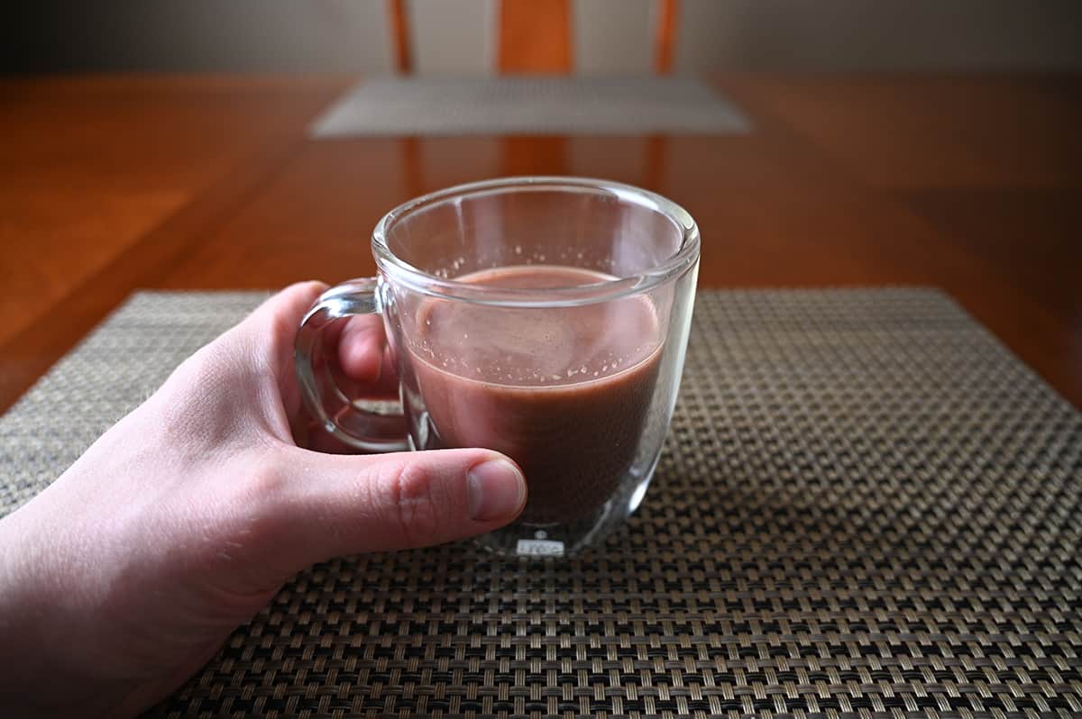 Closeup image of a hand holding a clear mug filled with candycane cocoa.
