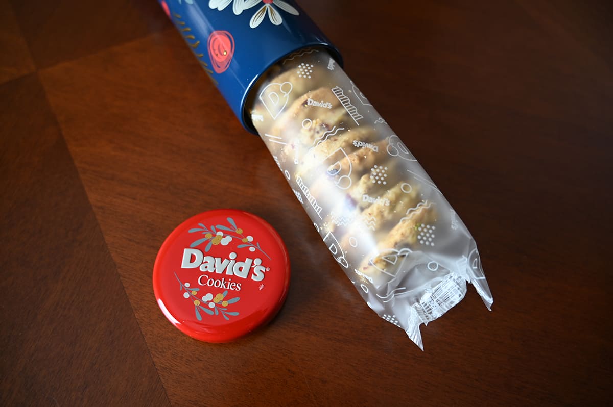 Image of the cookies coming half out of the tin with the lid for the tin beside the cookies.
