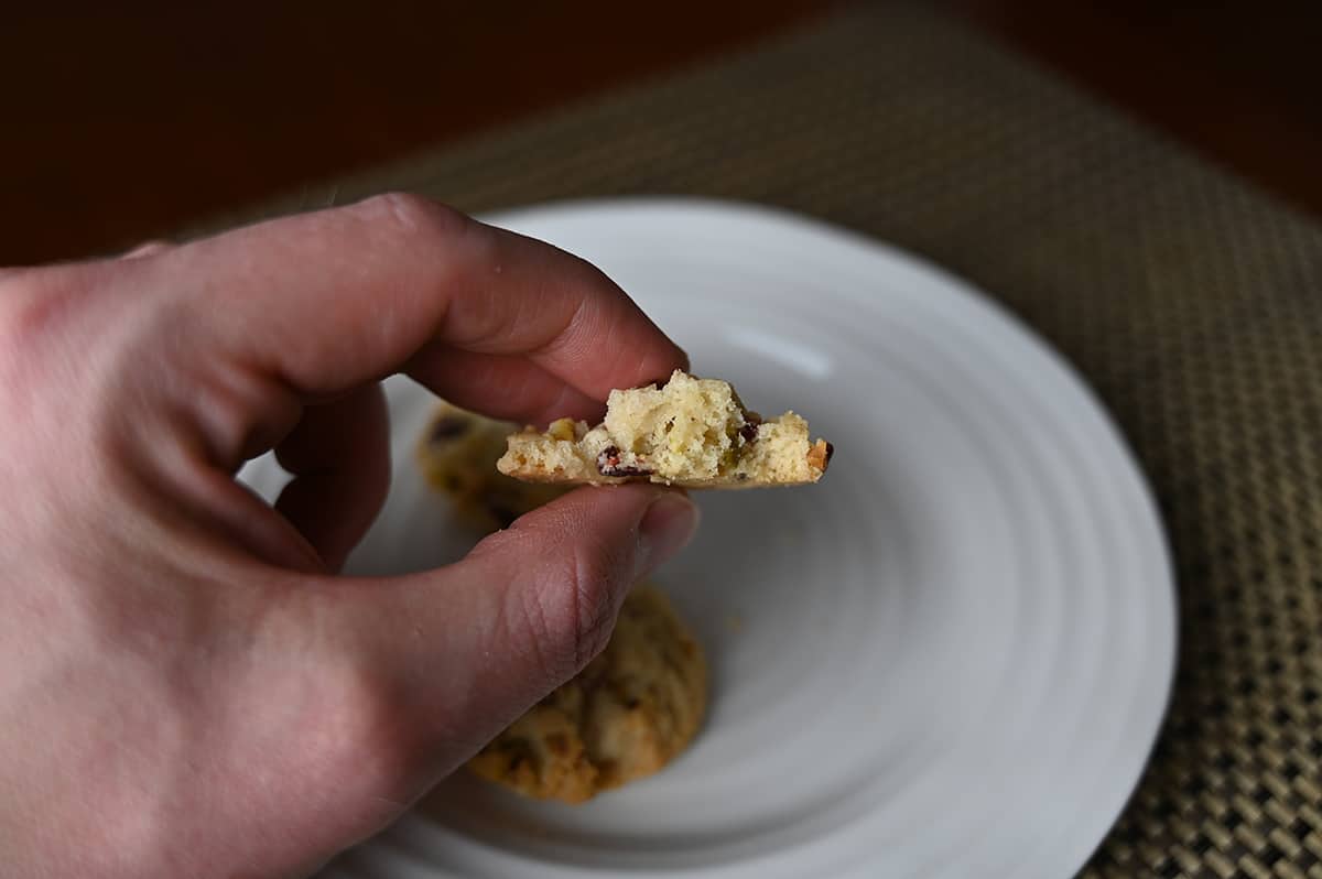 Side view image of a hand holding one cookie with a few bites taken out of it. 