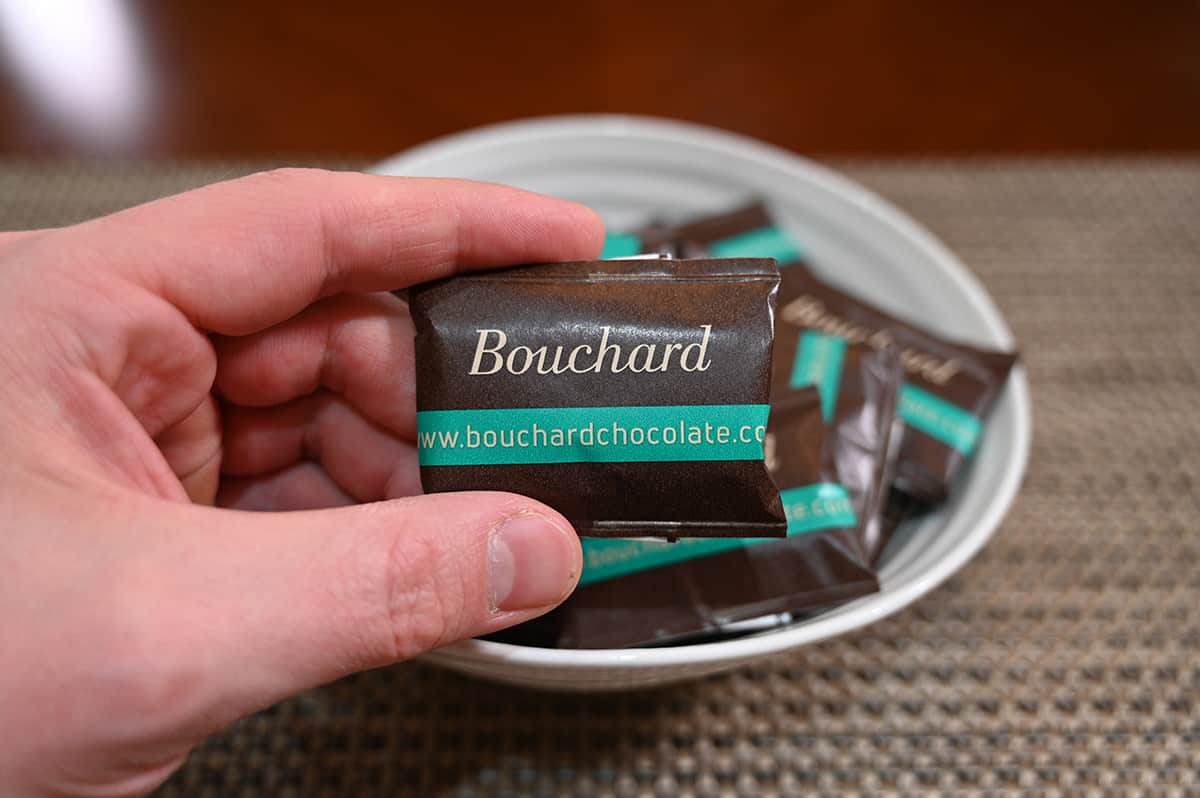 Image of a hand holding one individually wrapped mint chocolate close to the camera with a bowl of chocolates in the background.