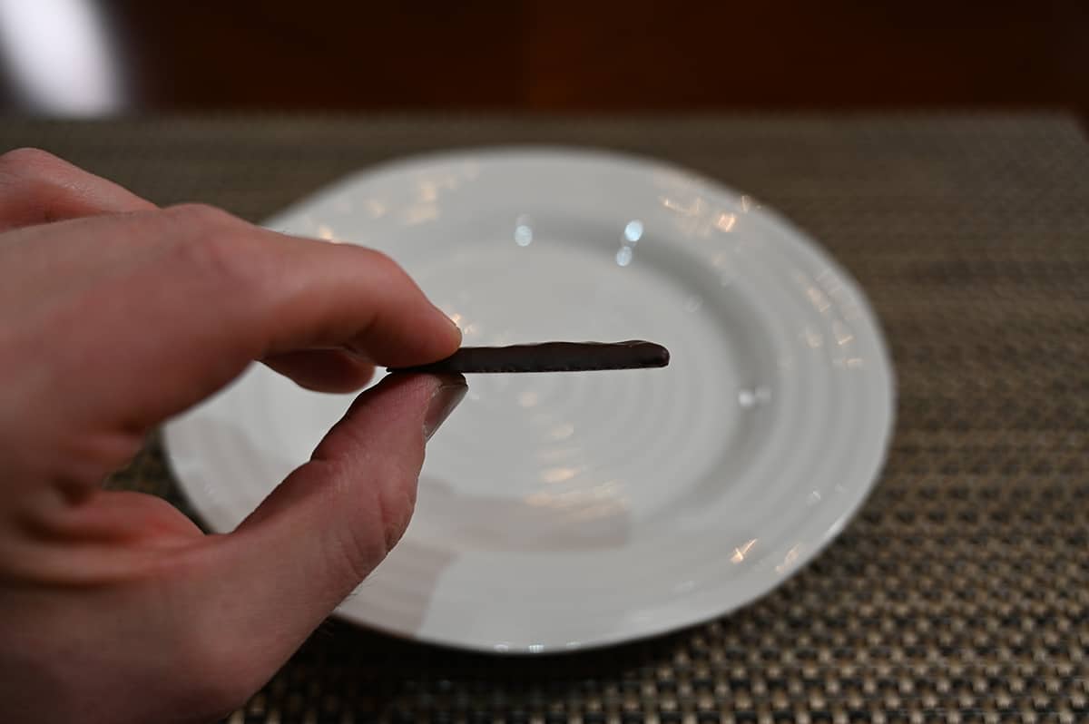 Image of a hand holding one mint chocolate close to the camera unwrapped on it's size so you can see how thick it is.