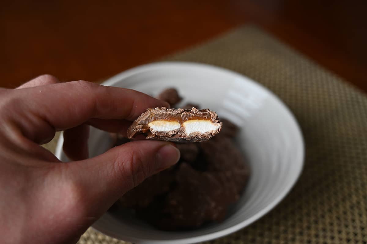 Closeup image of a hand holding one cluster close to the camera with a bite taken out of it so you can see the caramel and marshmallow.