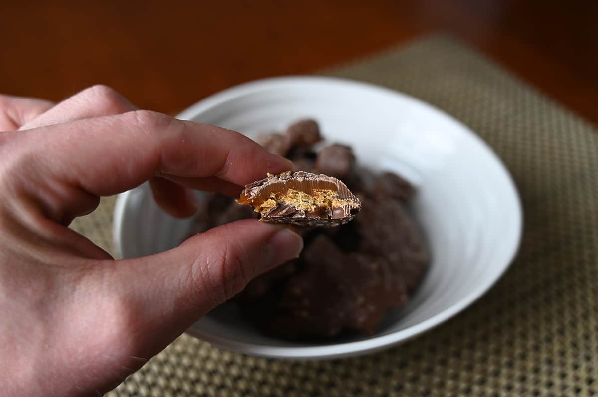 Sideview closeup image of a hand holding a cluster close to the camera with a bite taken out of it so you can see the graham crackers and caramel in it.