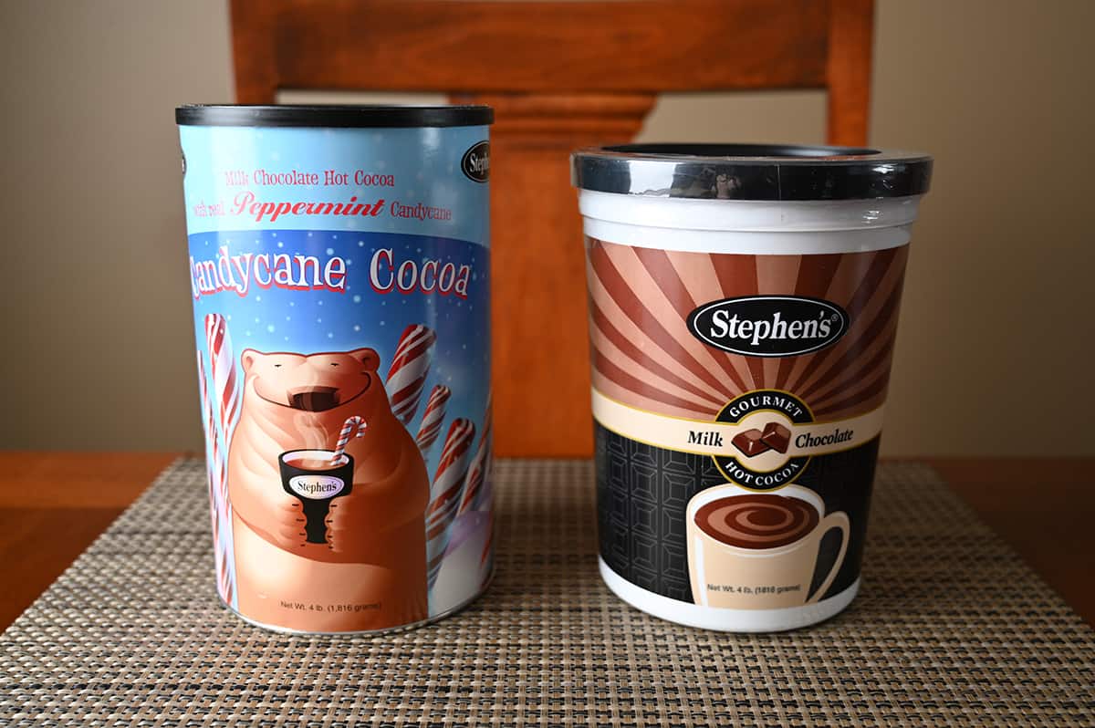 Image of two hot chocolate tubs unopened sitting on a table. One is candycane and the other is milk chocolate.