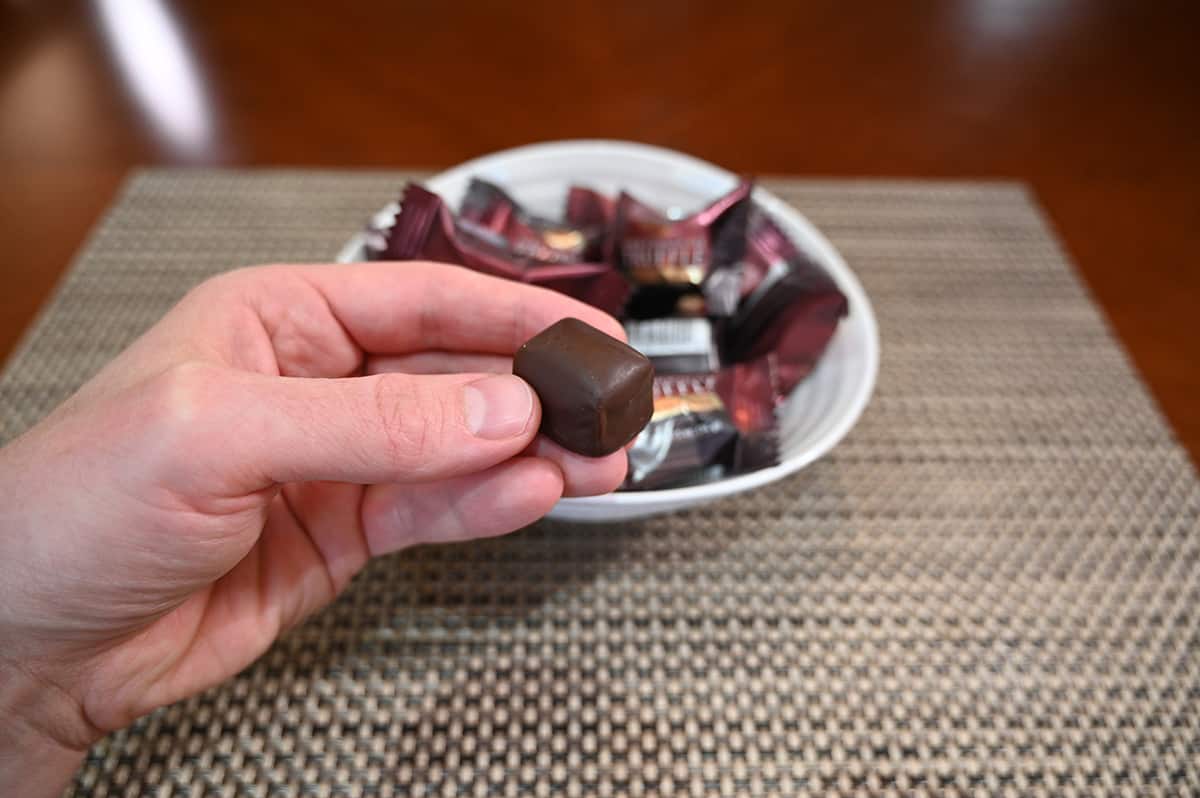Image of a hand holding one dark chocolate with sea salt truffle unwrapped over a bowl of wrapped truffles.