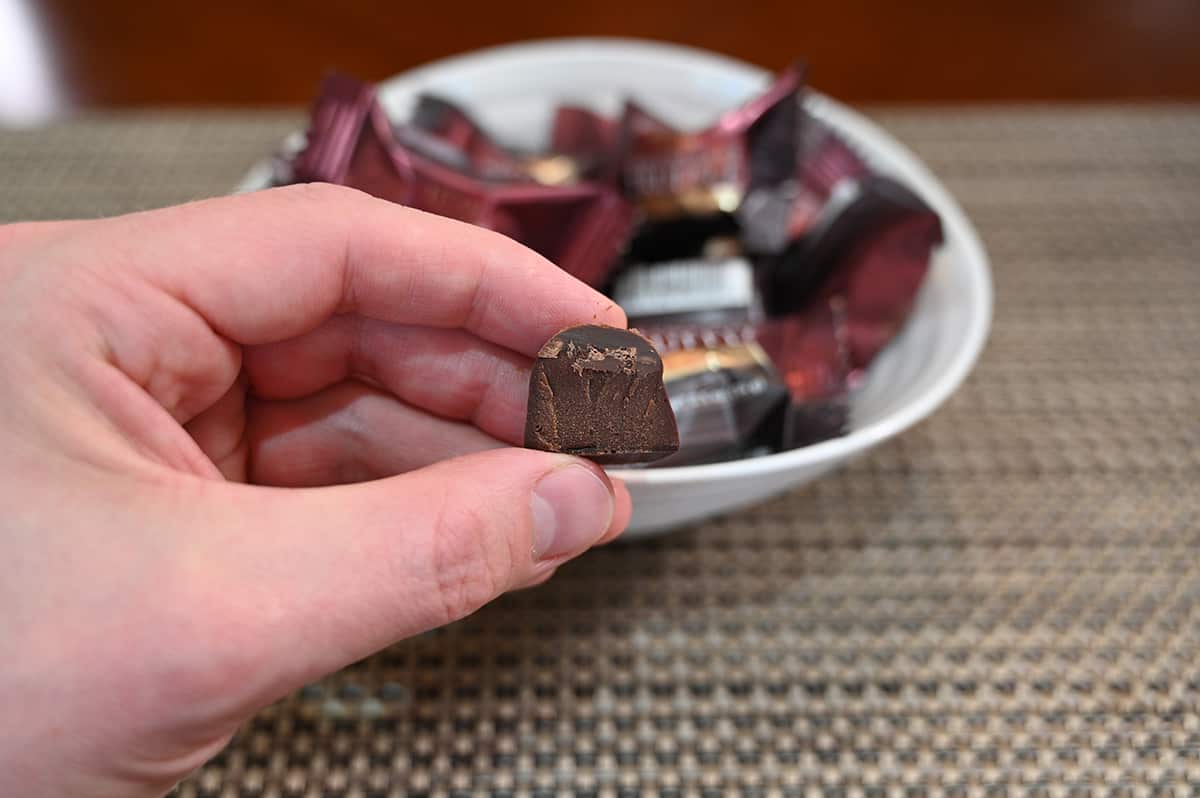 Image of a hand holding a dark chocolate with sea salt truffle unwrapped close to the camera with a bowl of wrapped truffles in the background.