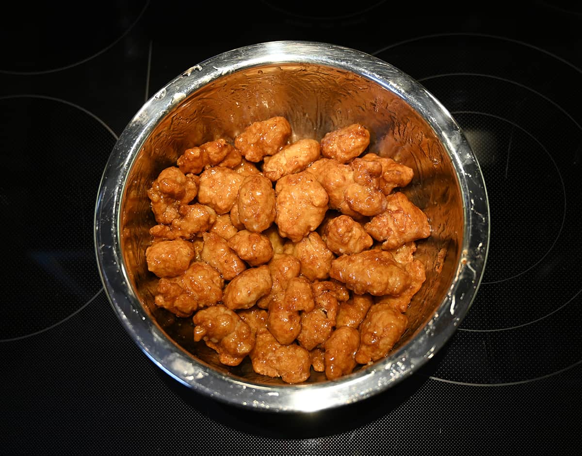 Top down image of a stainless steel bowl full of chicken after being tossed in the orange sauce.