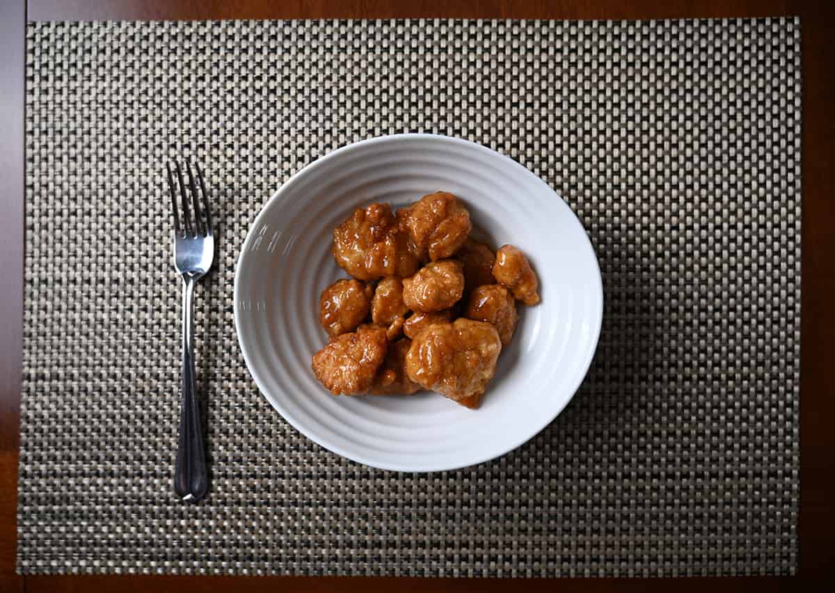 Top down image of a bowl of orange chicken served on a placemat with a fork beside the bowl.