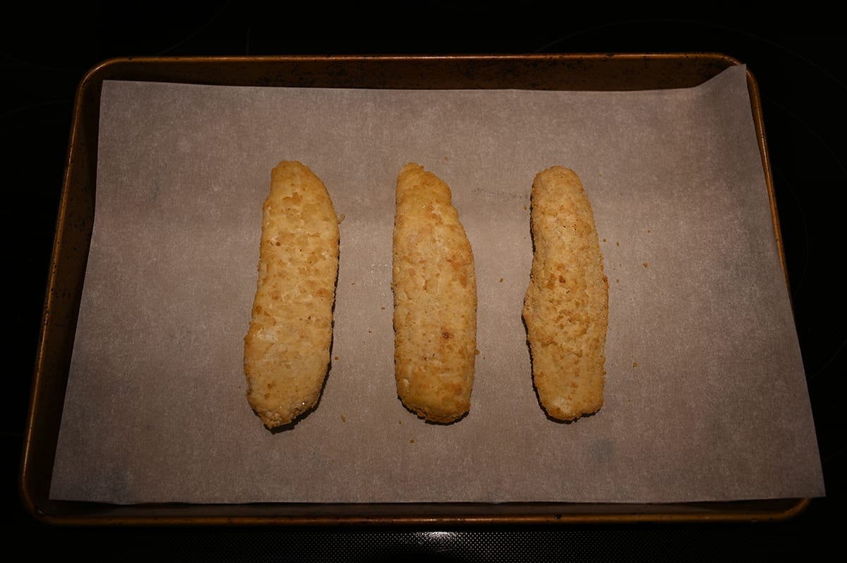 Image of three baked pieces of battered haddock  after being baked sitting on a parchment lined baking sheet. 
