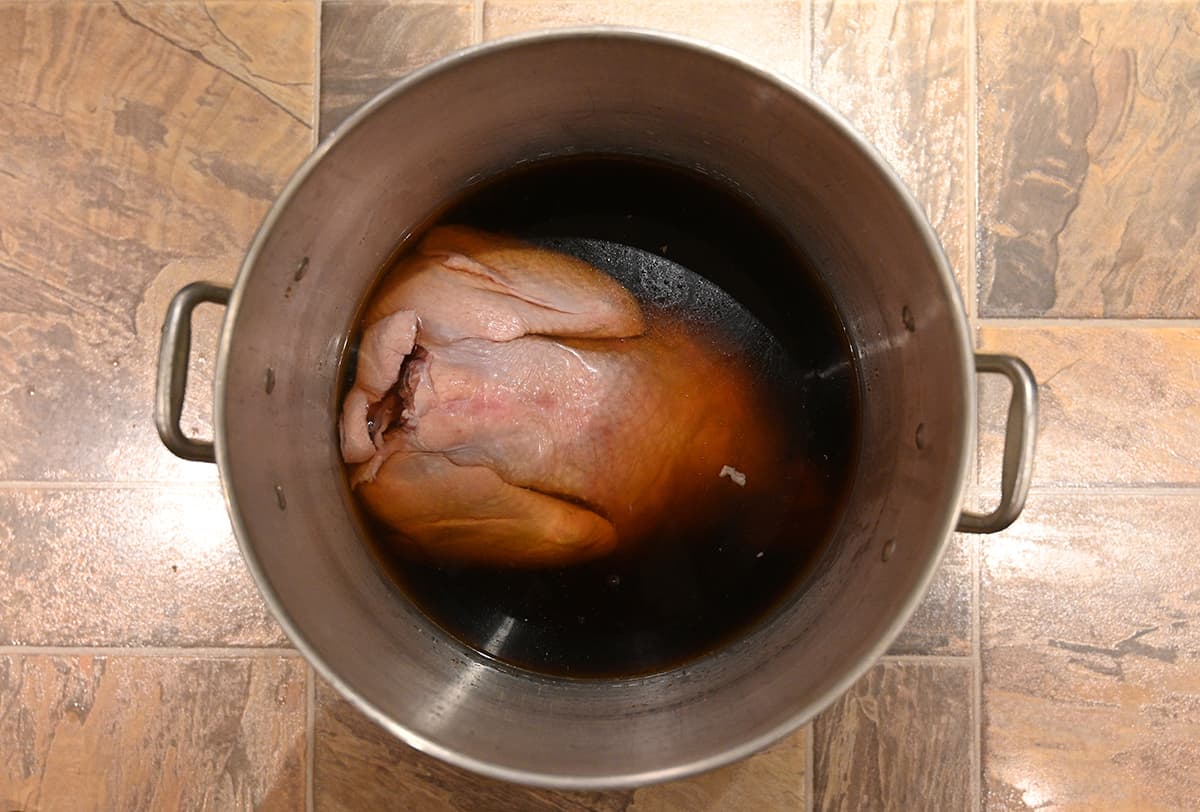 Image of a raw turkey sitting in a large pot full of brine. 