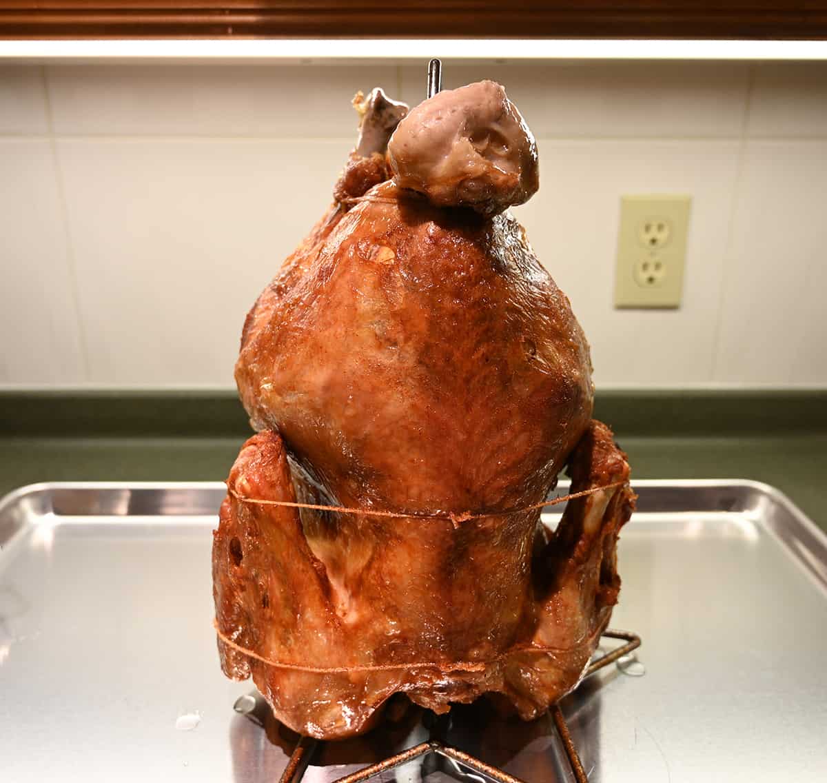 Image of a deep-fried turkey, fully cooked and golden brown sitting on a cookie tray before slicing.