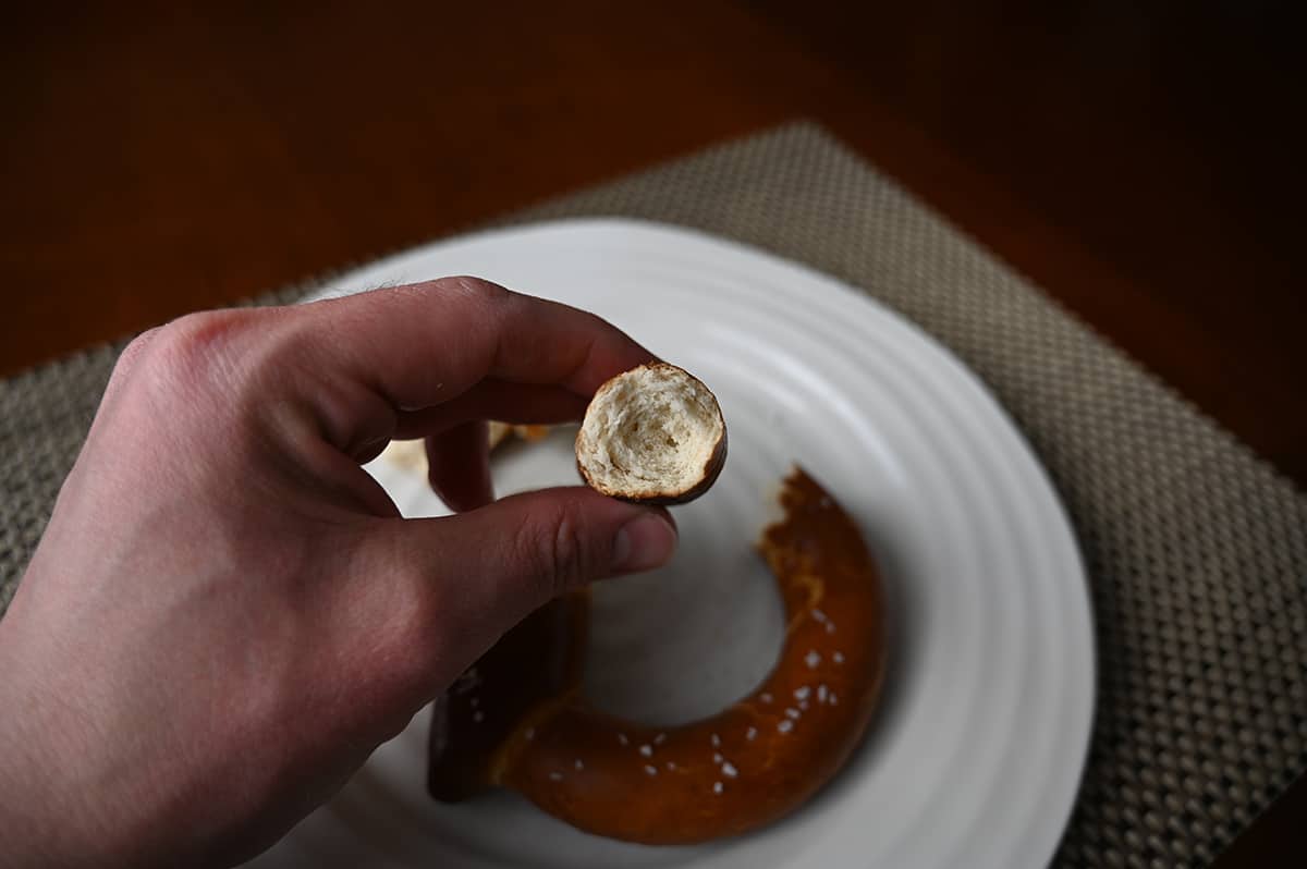 Image of a hand holding one soft baked pretzel with a bite taken out of it close to the camera so you can see the inside.