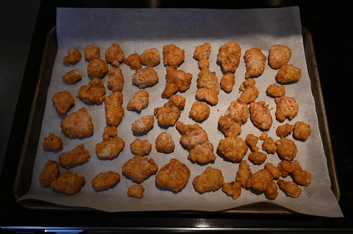 Image of breaded chicken pieces spread ot of a parchment lined baking sheet prior to being put in the oven.