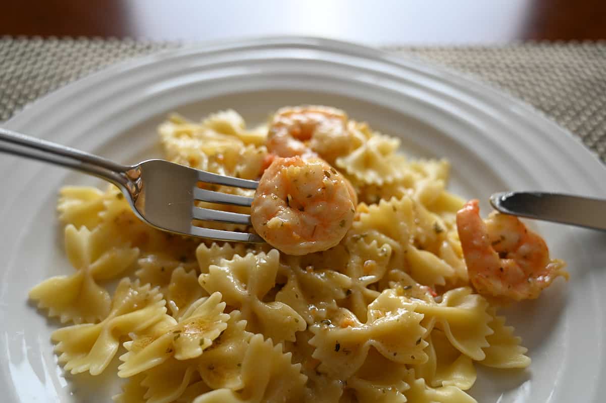 Closeup image of a plate of bow tie pasta with garlic butter shrimp, a fork is hovering over the plate with a shrimp on it.