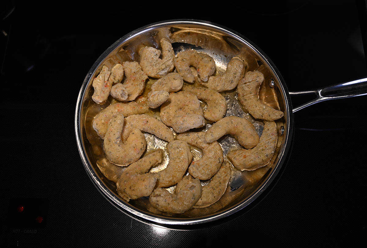 Top down image of a pan on a stovetop with the shrimp starting to be sauted in the pan.