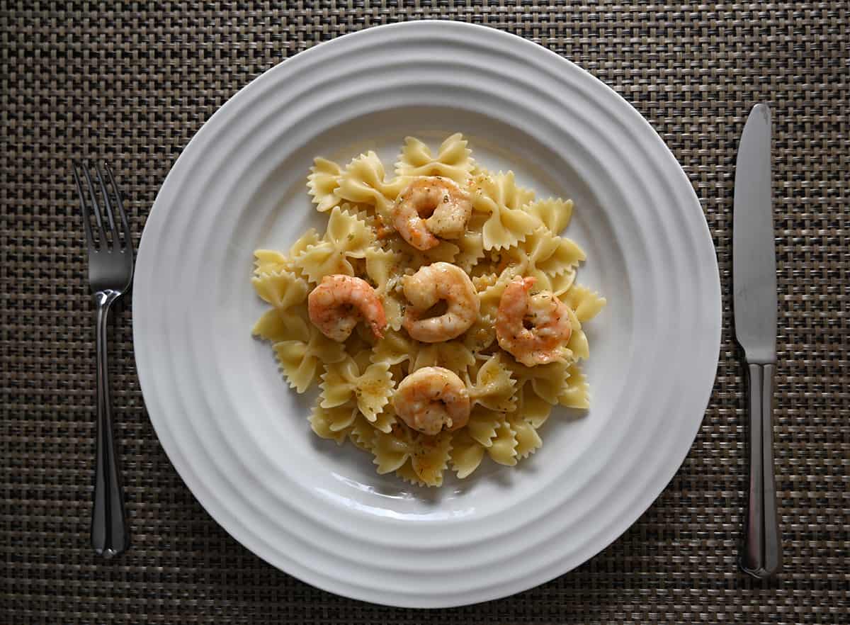 Top down image of a plate of pasta served on a white plate, on top of the bow tie pasta is shrimp.