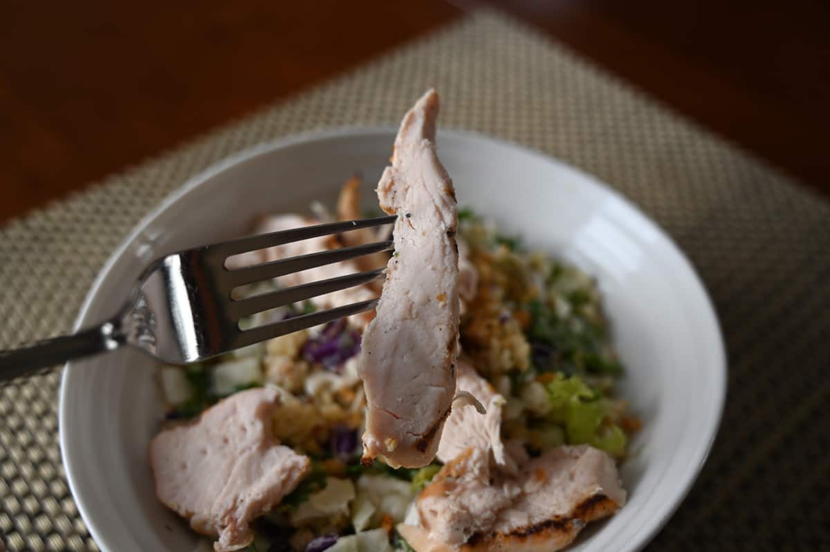 Image of a fork holding one chicken strip overtop a bowl of salad with chicken on the salad.