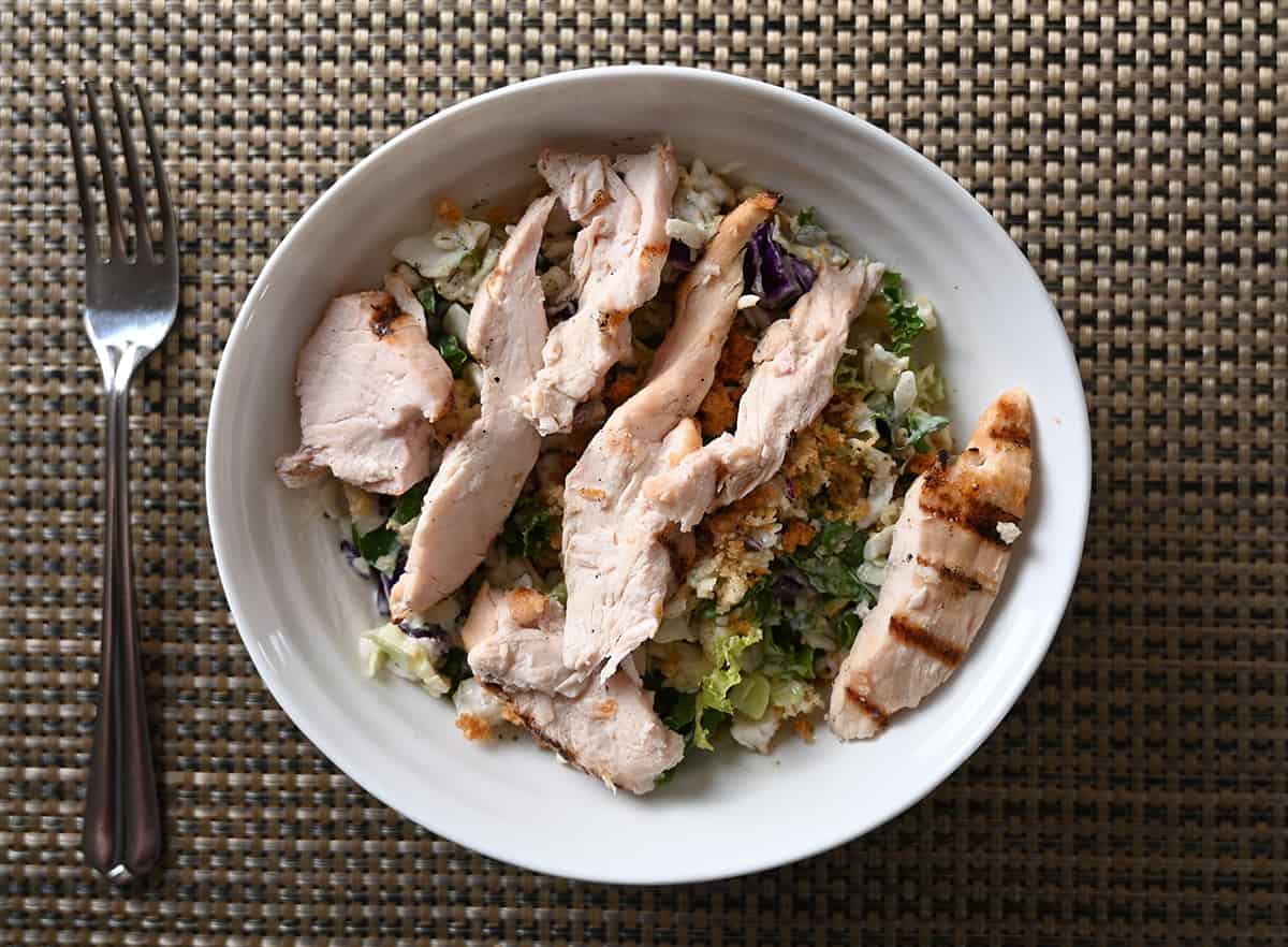 Top down image of a bowl of salad with chicken on top of the bowl. 