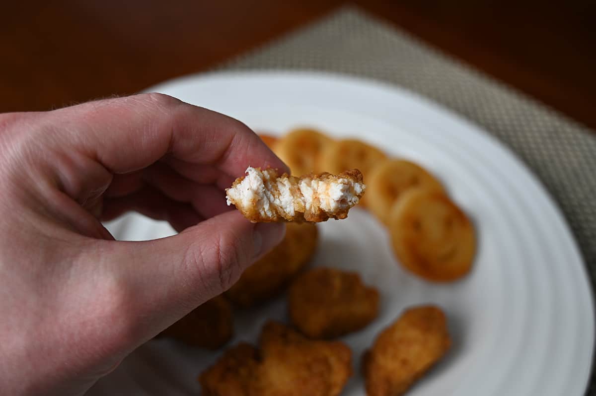 Closeup image of  a hand holding one chicken breast chunk close to the camera with a bite taken out of it so you can see the center.