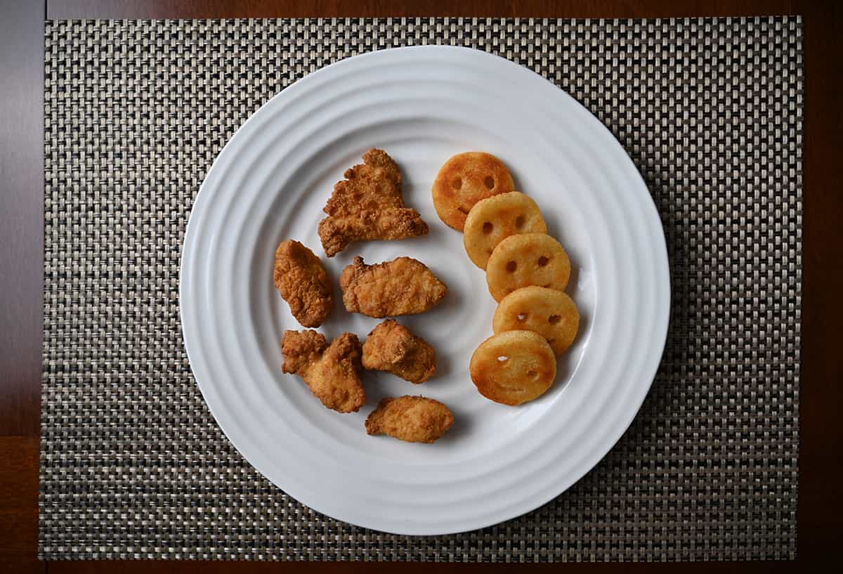 Top down image of a white plate with chicken breast chunks served beside smiley fries.