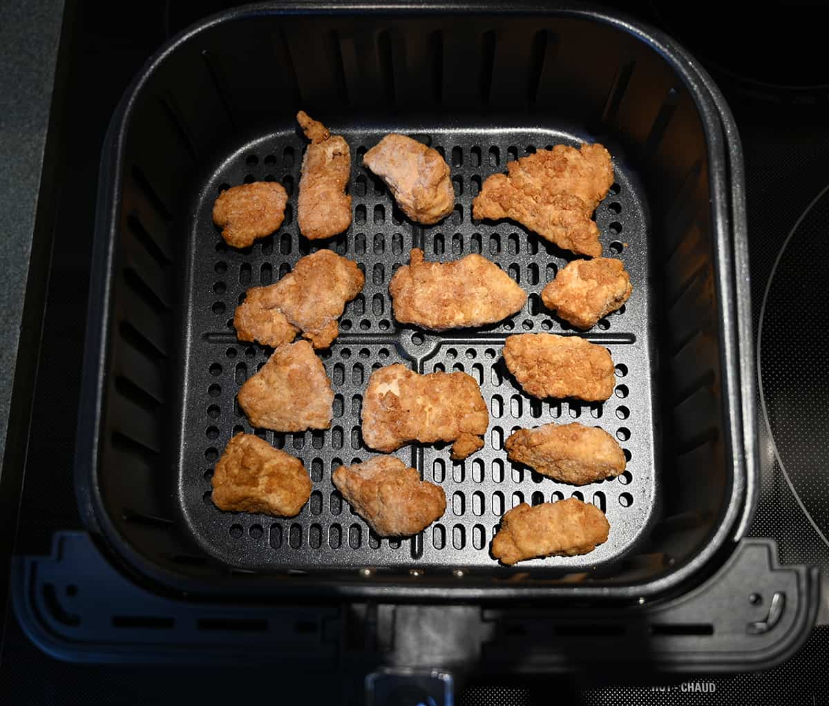 Top down image of an air fryer tray with heated chicken breast chunks in it.
