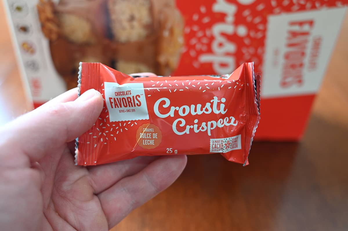 Image of a hand holding one Crispeez Square individually packaged in front of the camera.