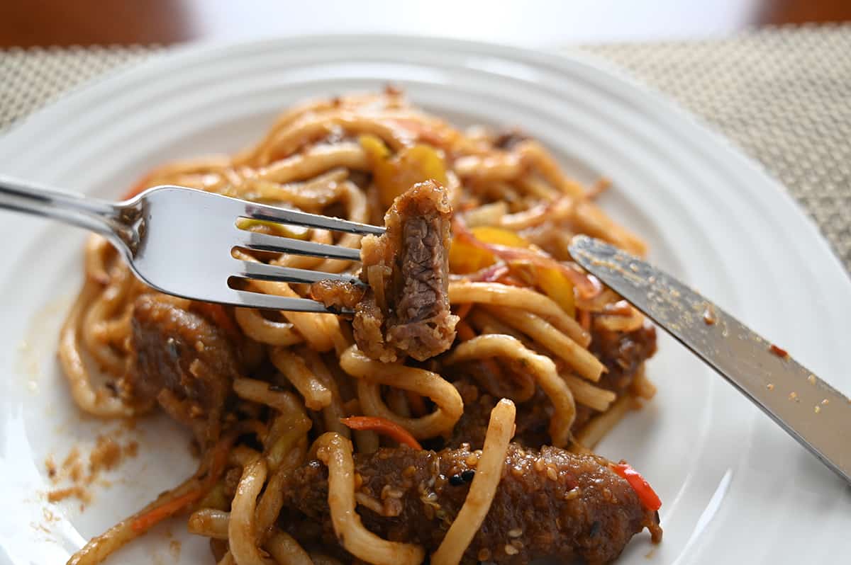 Side view close up image of a plate of ginger beef stir fry and a fork close to the camera with a piece of beef on it.