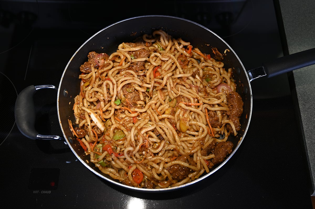 Top down image of a pan with noodles and ginger beef after being combined and cooked on the stovetop.