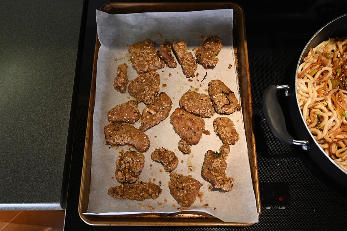 Top down image of a parchment lined cookie sheet with cooked ginger beef on it out of the oven.