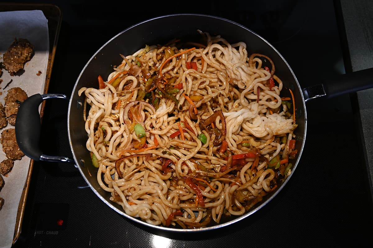 Top down image of a pan with noodles and ginger beef cooking in it on the stovetop.