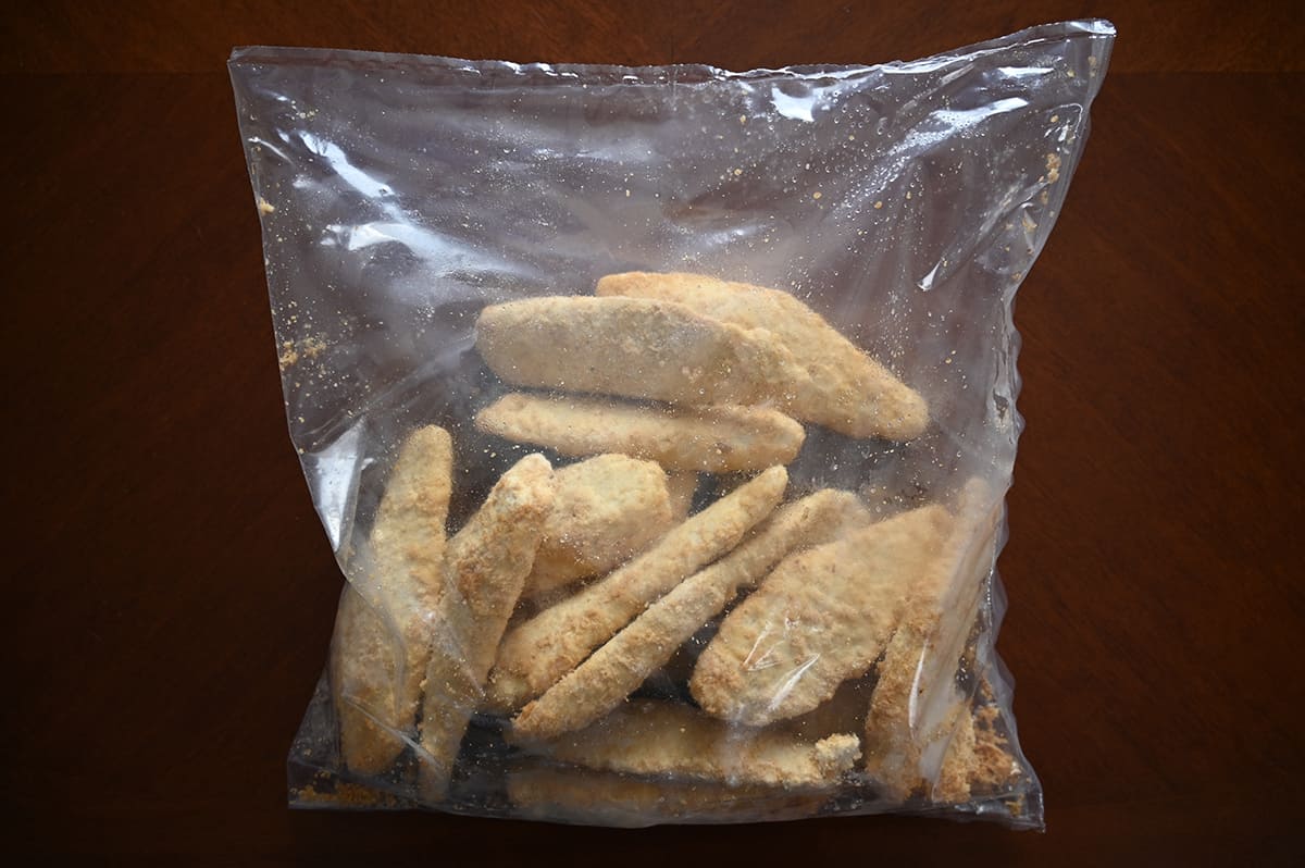Top down image of a clear plastic bag with frozen fish sticks in it sitting on a table unopened.