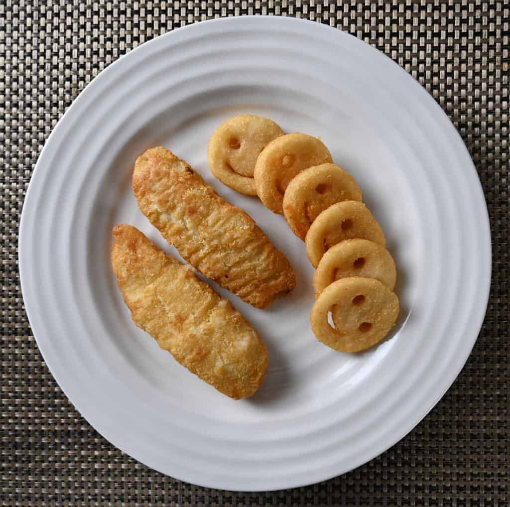 Top down image of a white plate with two pieces of fish served on it beside a side a fries.