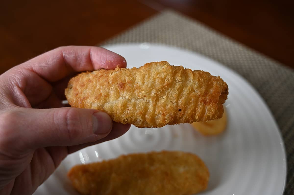 Image of a hand holding one piece of baked battered haddock close to the camera. 