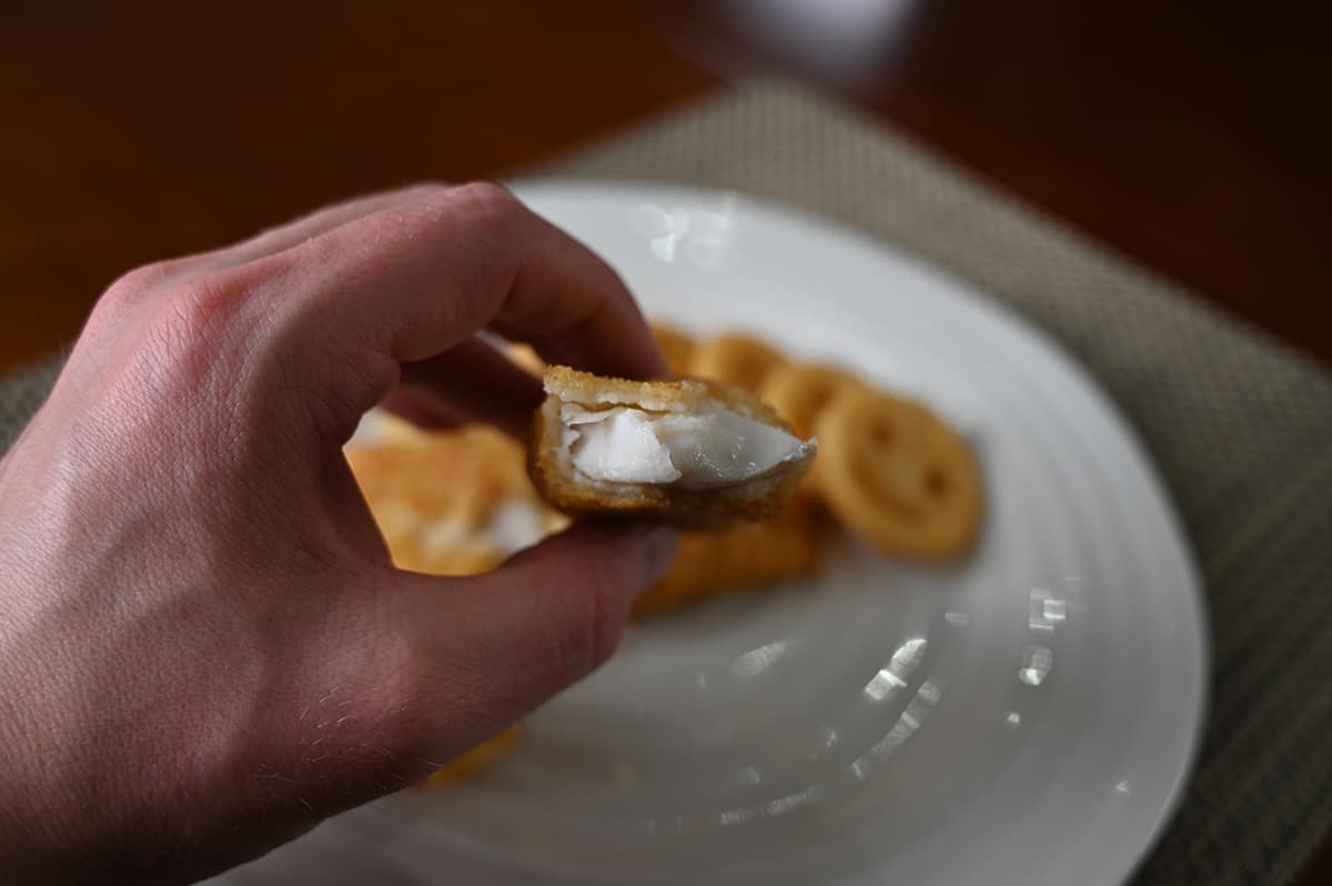 Closeup image of a hand holding one cooked battered piece of haddock close to the camera with a bite taken out of it so the center is visible.