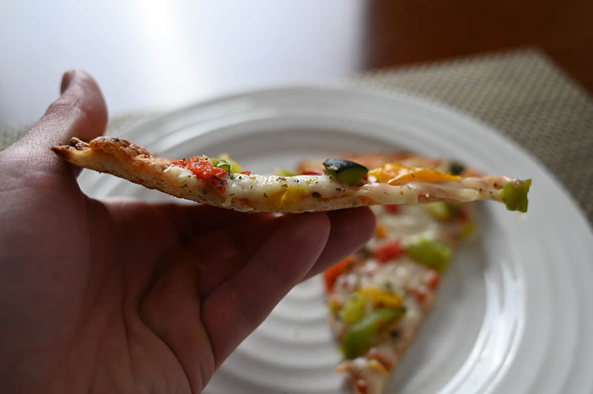 Closeup sideview image of a hand holding one slice of pizza close to the camera so you can see how thick the crust is.