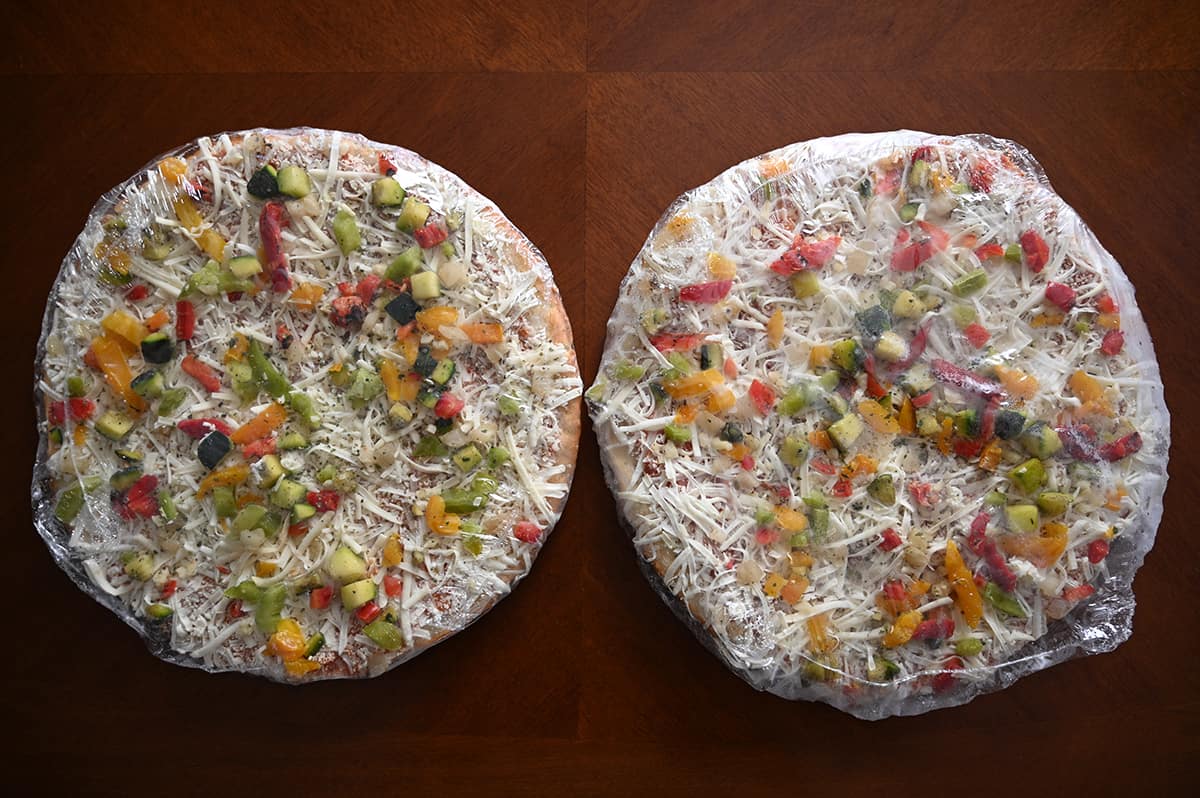 Image of two frozen pizzas wrapped in plastic sitting on a table.