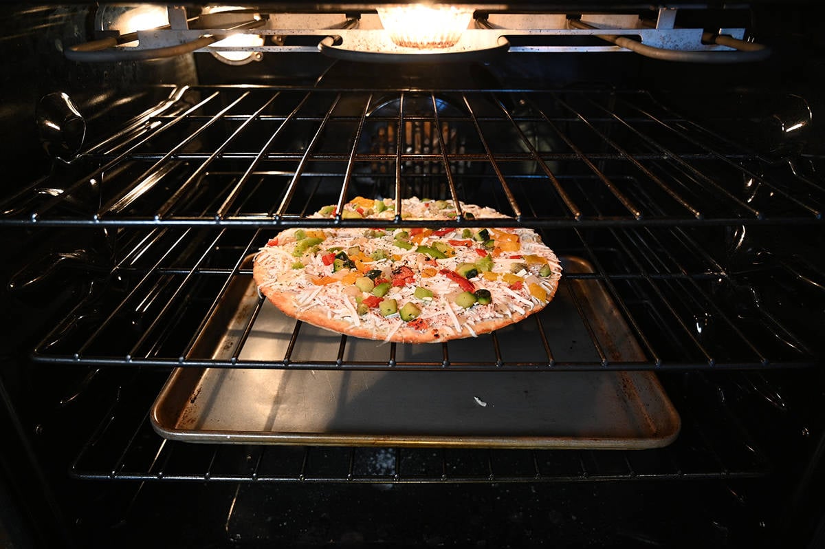 Image of a pizza inside an oven baking on the middle rack, on the rack below is a cookie sheet.