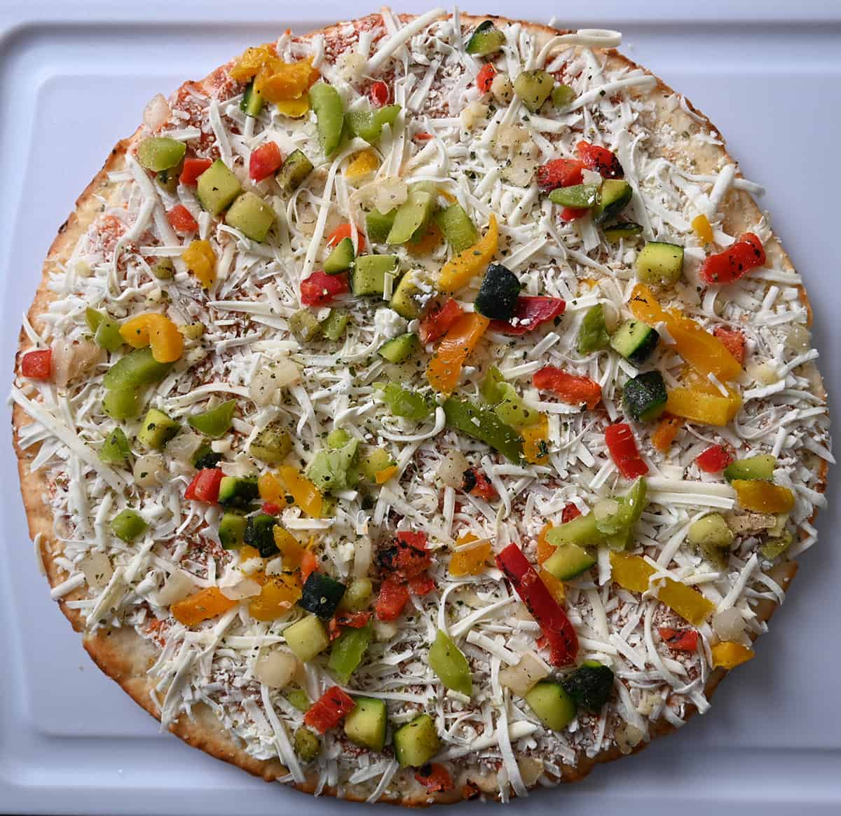 Top down image of the cauliflower crust pizza frozen on a cutting board before baking it.